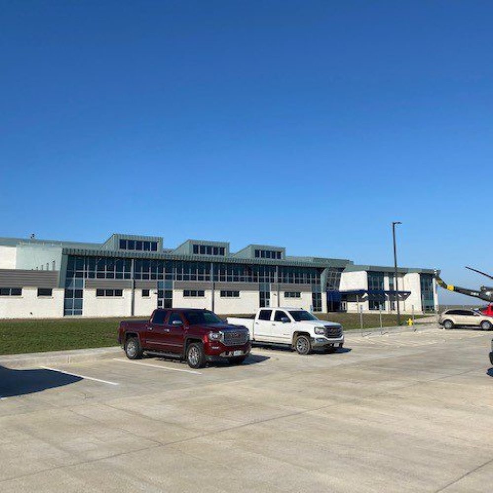 Exterior view from parking lot of TASMG READINESS CENTER with helicopter beside building